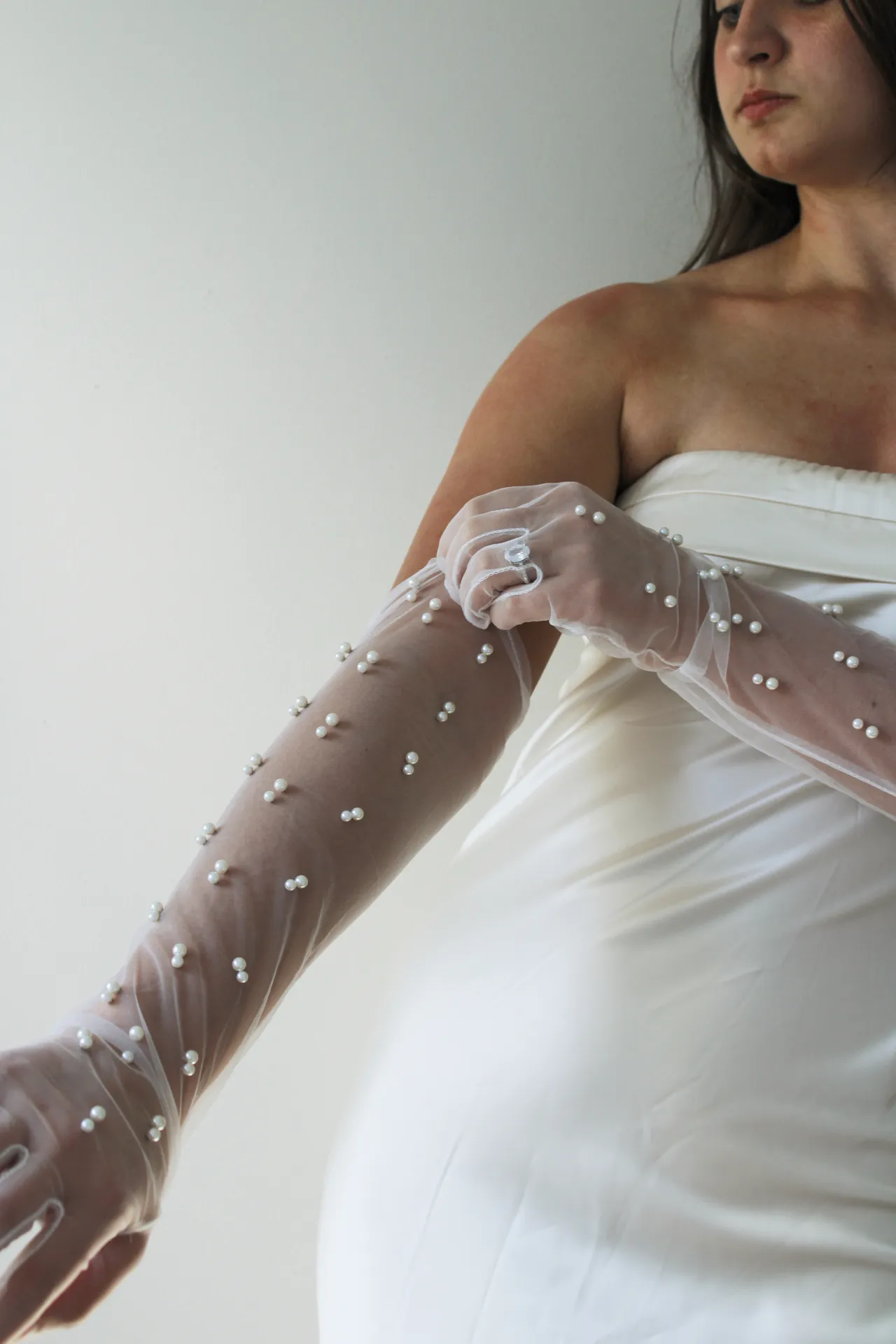 Person in a white dress adjusting a pearl-covered glove