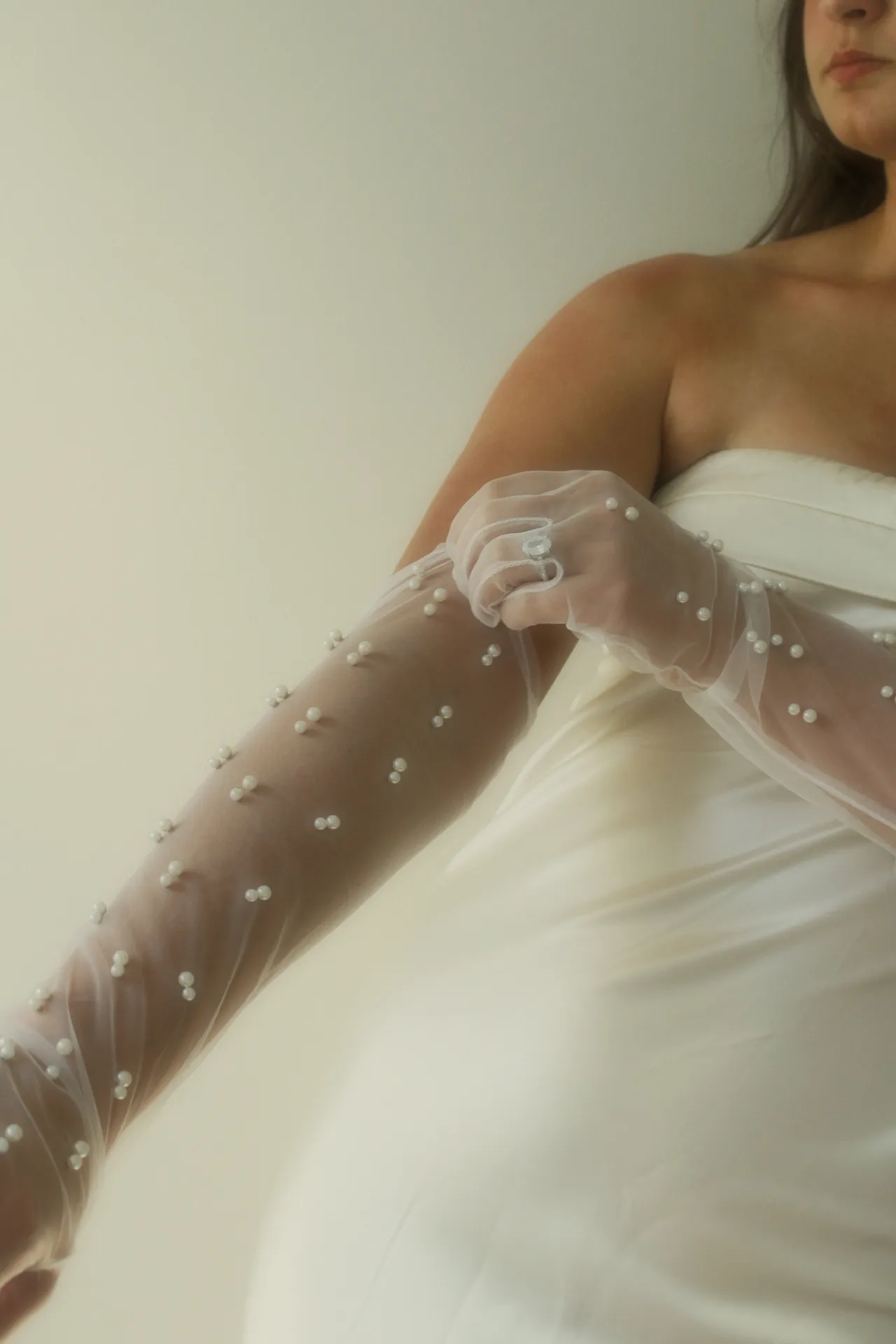 Person in a white dress adjusting a pearl-covered glove